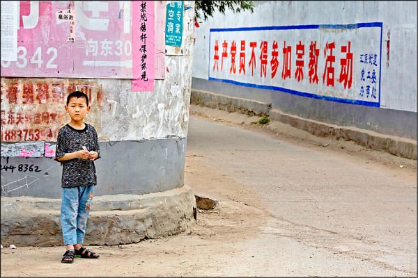 中國河南省平頂山市一名男孩站在一座教堂附近，牆上寫有「共產黨員不得參加宗教活動」標語。（美聯社檔案照）