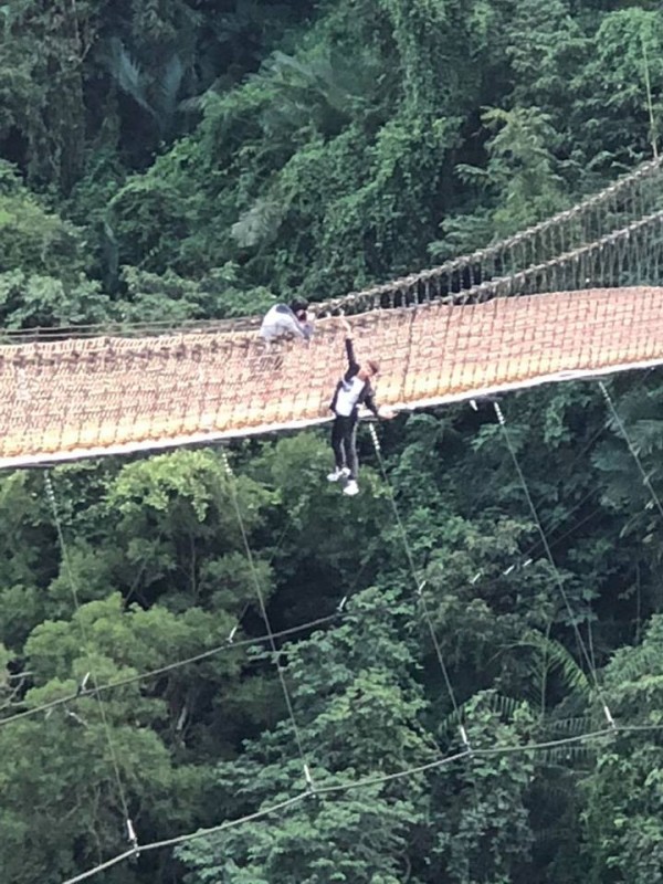 一名年輕男子為了拍照，竟只用一隻手抓住吊橋護繩，整個身體翻出吊橋外「懸掛」在橋上。（圖擷自爆料公社）
