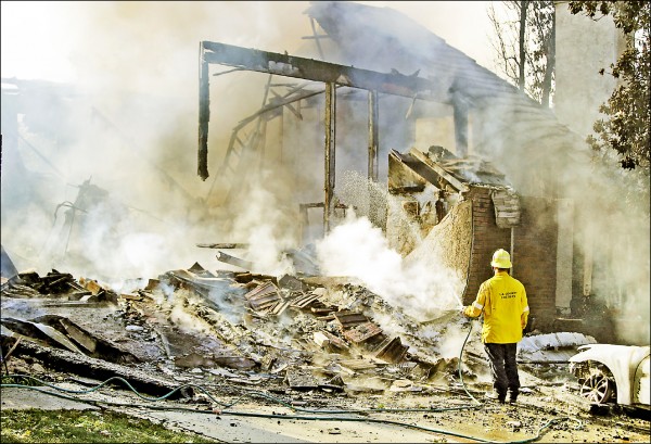 加州阿古拉地區的消防人員朝仍在燜燒的房屋灑水。（歐新社）