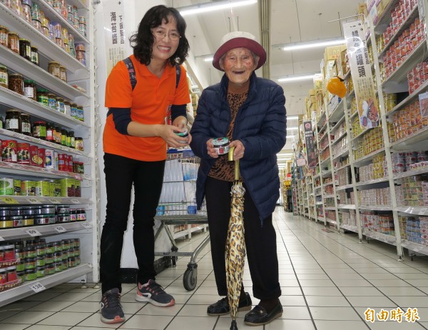 95歲阿嬤陳雪花拄著雨傘由志工攙扶選購衛生紙、海苔醬等日常用品。（記者湯世名攝）