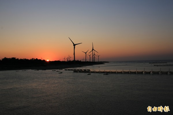 玄寶大橋跨越中港溪出海口，每逢夕陽西下，落日沒入山頭，印襯一旁的發電風車及漁船景致，吸引許多攝影愛好者搶拍。（記者鄭名翔攝）