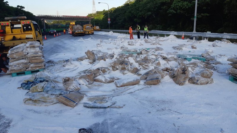 載滿水泥包的貨車在國道3號汐止段南下匝道翻覆，水泥包散落佔用車道，嚴重影響交通。（圖由新北市交通局提供）