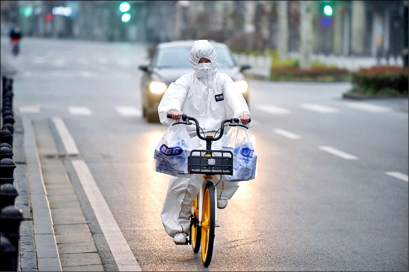 武漢街頭一人穿著隔離衣騎車採買物資。（法新社）