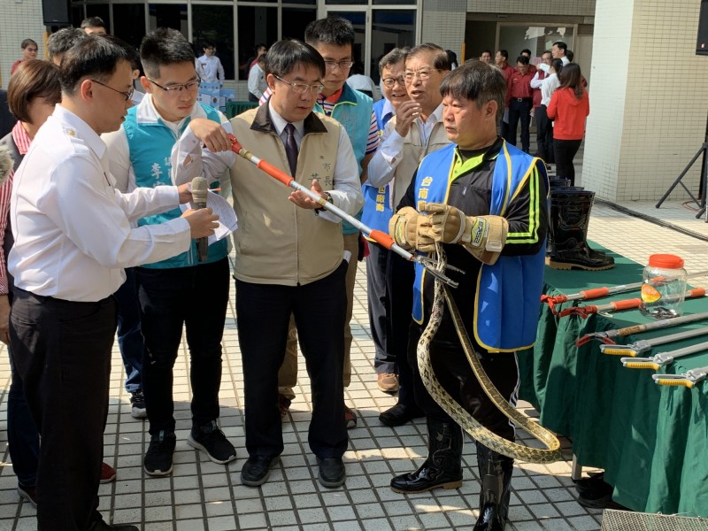 台南市長黃偉哲（中）在民間捉蛇員的協助下體驗拿工具捉蛇的過程。（記者王俊忠翻攝）