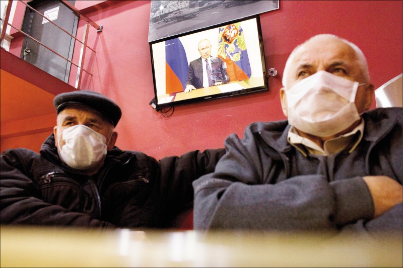 俄羅斯首都莫斯科疫情緊張，總統普廷下令首都非必要商店、公園關閉一週，修憲公投也因此延後。莫斯科一家咖啡店裡，戴著口罩的顧客二十五日看普廷的電視演說。（彭博）