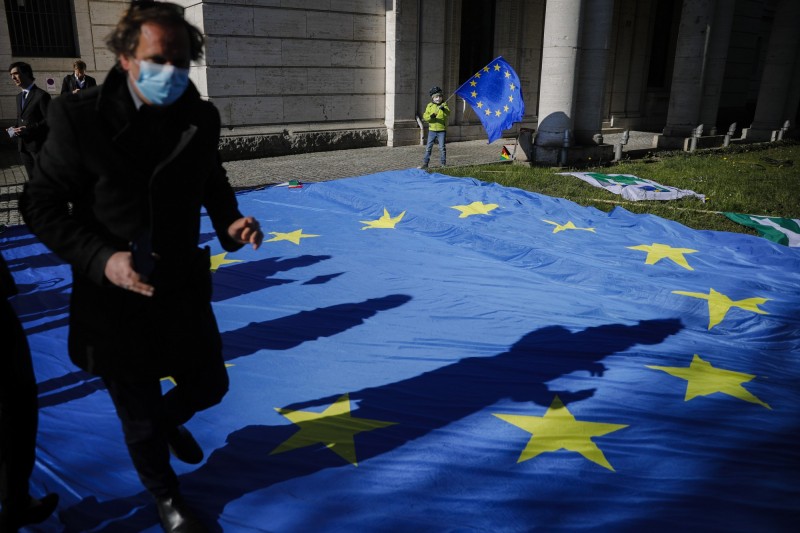 歐洲部分國家疫情日前雖稍有緩和，但近期似有新一波疫情爆發。德國今（22）日再傳2237例確診、281人死亡；西班牙則新增4211例確診、435例死亡。圖為歐洲民眾配戴口罩經過歐盟旗幟。（美聯社）