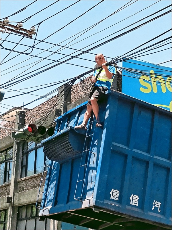 謝景隆爬上二層樓高大卡車車斗，以膠帶將電線綑綁住，讓里民得以安全通行。（記者陳文嬋翻攝）