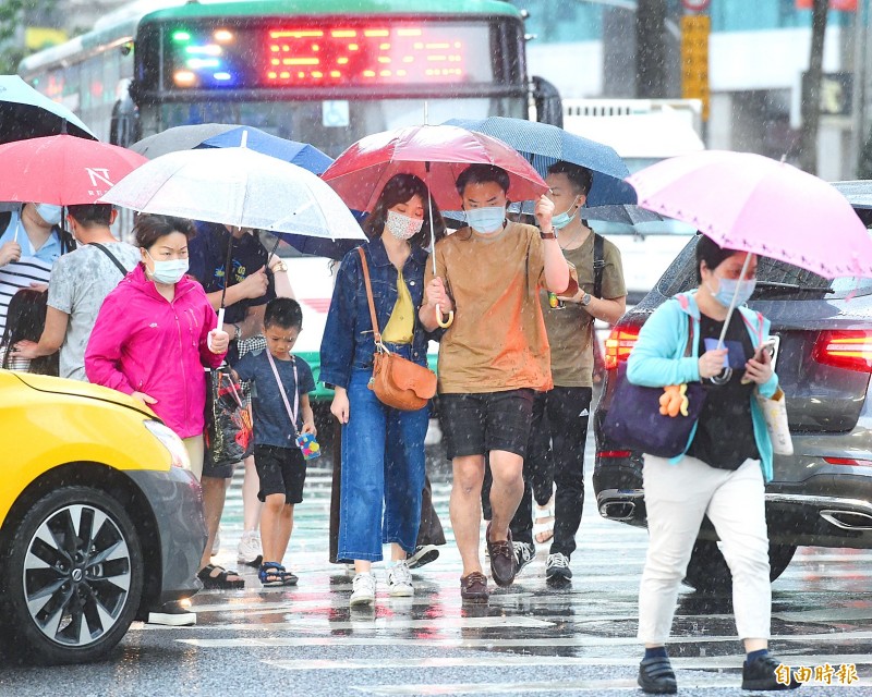 People cross a streeet holding umbrellas to shield themselves from heavy rain in Taipei yesterday afternoon.
Photo: Fang Pin-chao, Taipei Times