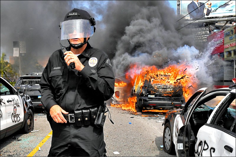美國暴動持續延燒，洛杉磯警察指揮官站在被塗鴉、炸毀的警車旁，繼續指揮鎮壓。
（美聯社）