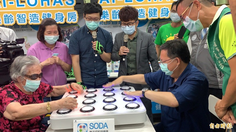 市長鄭文燦（右）坐下和95歲阿嬤在類似打地鼠的按燈遊戲「SODA─手眼協調」中對戰，最後由阿嬤獲勝。（記者陳恩惠攝）