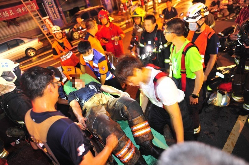 受傷的消防員臉部表情糾結，被抬上擔架送醫。（記者王捷攝）