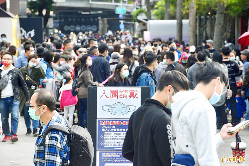 Visitors wearing masks yesterday crowd a Taipei park, where a sign at the entrance reminds people to wear masks at eight types of public venues to prevent the spread of COVID-19.
Photo: George Tsorng, Taipei Times