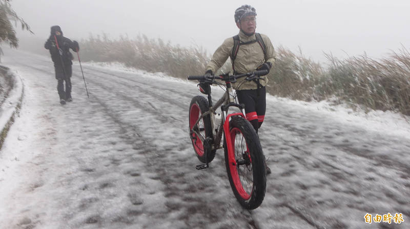 不少遊客騎單車上山賞雪，不過由於路面結冰濕滑，多數時間必須下車牽行。（記者劉信德攝）