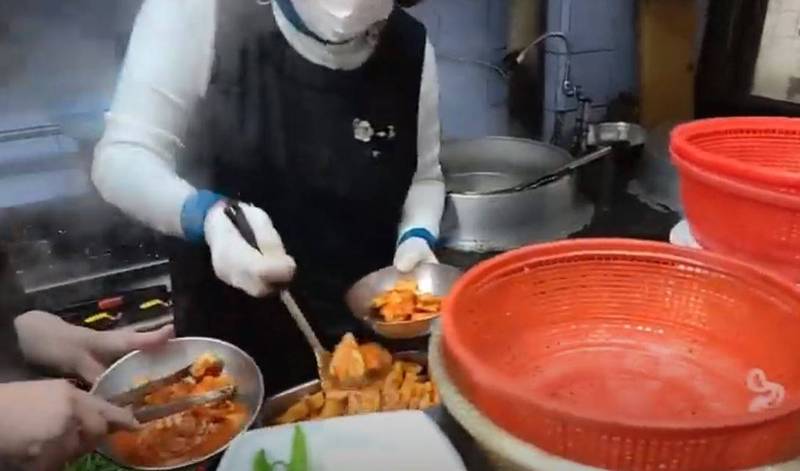 南韓正妹實況主康多昷在姑母家開的豬肉湯飯餐廳直播，無意間拍到員工回收客人吃剩的蘿蔔泡菜又繼續賣給別人的影像。圖片左方為員工將蘿蔔泡菜夾回容器裡，中間為職員從同一容器挖出泡菜準備端給客人。（圖擷自「이슈코리아」YouTube）