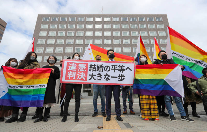 北海道札幌地方法院今日判決出爐，認為不承認同性婚姻實屬違憲，支持同性婚姻的平權人士在法院外持標語及彩虹旗慶祝。（法新社）