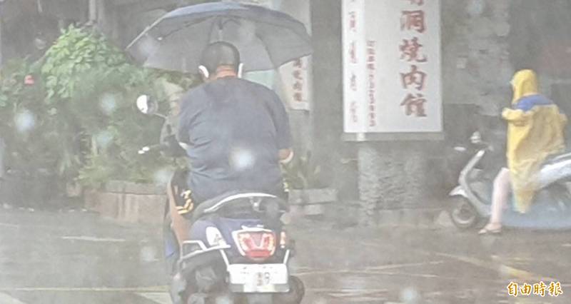 屏東平頭男在大雨中單手騎機車、撐傘還抽煙，行為有夠離譜。（記者葉永騫攝）