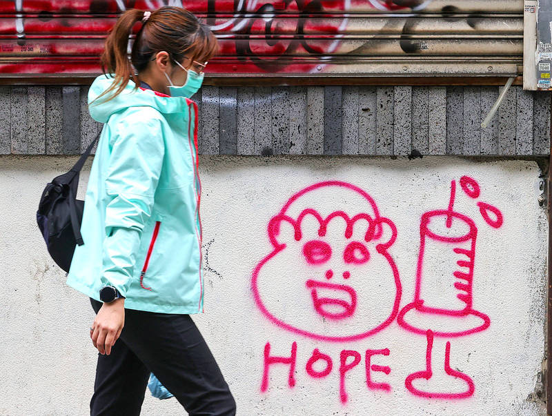 A woman yesterday walks past a graffito in a lane in Taipei’s eastern district. The need for vaccines has become urgent in Taiwan amid a domestic COVID-19 outbreak that started in earlier this month.
Photo: CNA