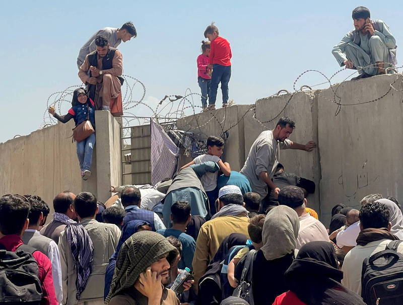民众聚集在喀布尔机场外试图翻墙进入搭上离开阿富汗的飞机，画面中有人正帮助女孩爬上围墙。（法新社）(photo:LTN)