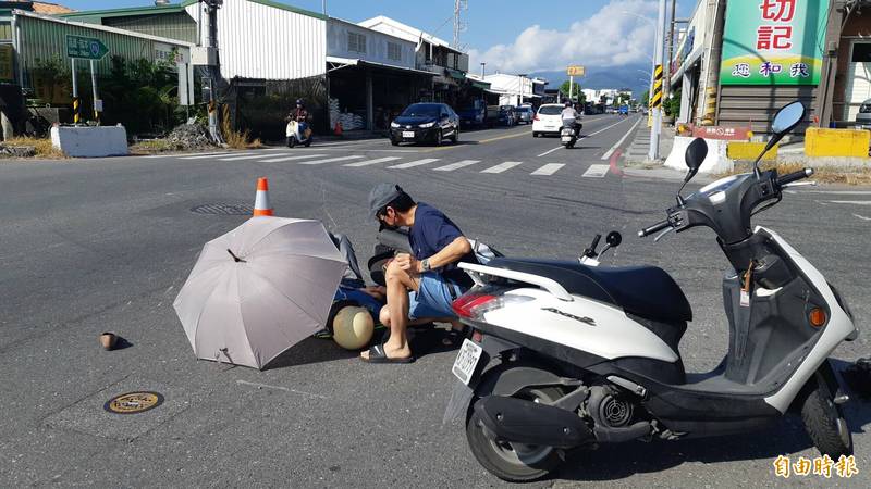 台東市中華路與四川路交叉口上午發生2機車相撞事故，一婦人倒在馬路上，附近店家為她架傘遮陽，她的丈夫也趕來護妻。（記者黃明堂攝）