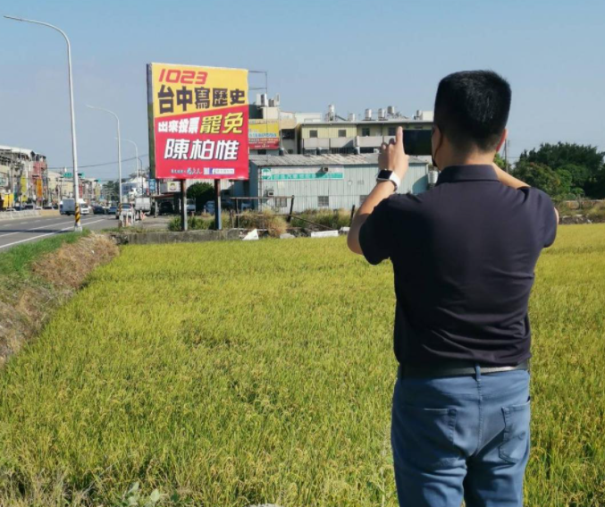 顏寬恒手持手機，似乎想拍下遠處一塊罷免陳柏惟的看板，但是手機螢幕卻是一片黑。（擷取自顏寬恒臉書）