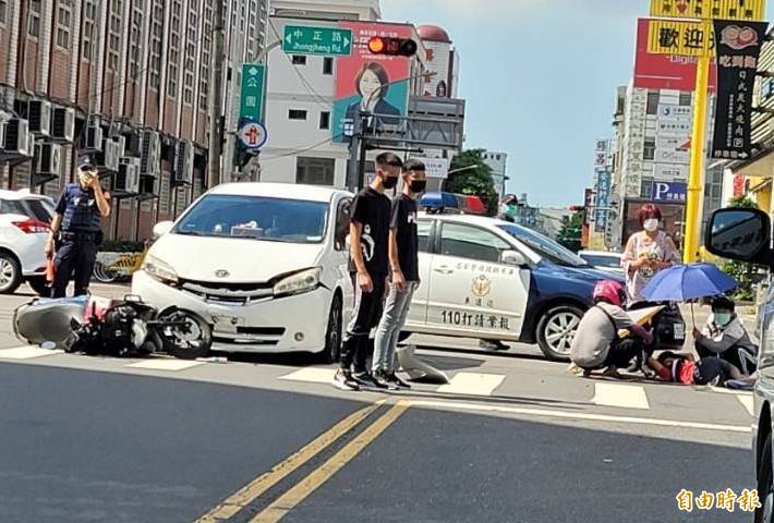 屏東太平洋百貨公司大門前交叉路口發生車禍，熱心民眾撐傘護傷者。（記者葉永騫攝）