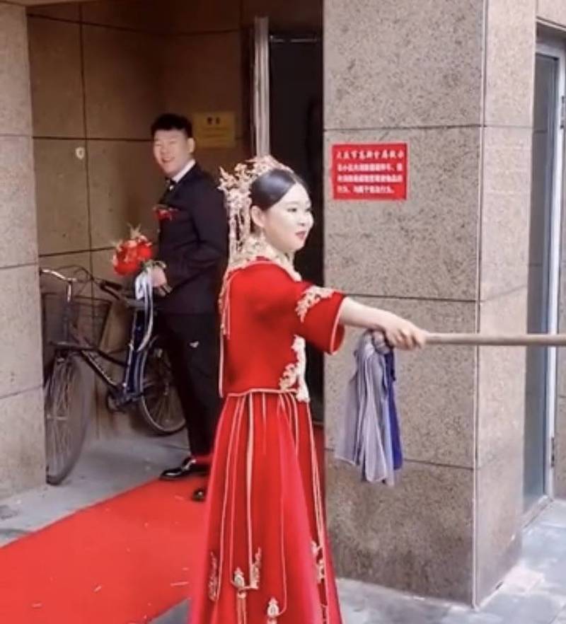 中国黑龙江大庆一名新娘挥舞着拖把「霸气护夫」，阻止朋友们婚闹，而新郎则在新娘背后偷笑，画面十分逗趣。（图取自微博）(photo:LTN)