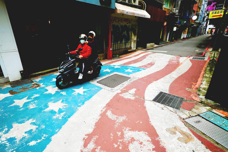 People ride a scooter over a painting of a US flag on a street in Taipei yesterday after the administration of US President Joe Biden invited Taiwan to its Summit for Democracy next month.
Photo: RITCHIE B. TONGO, EPA-EFE