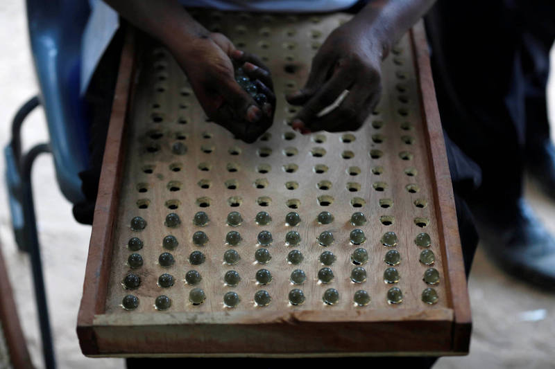不是夜市彈珠枱！甘比亞總統大選的投票方式是放置玻璃彈珠到候選人投票箱中。圖為甘比亞總統大選後，選舉人員用有孔洞的泥板在算票箱彈珠票數。（路透）