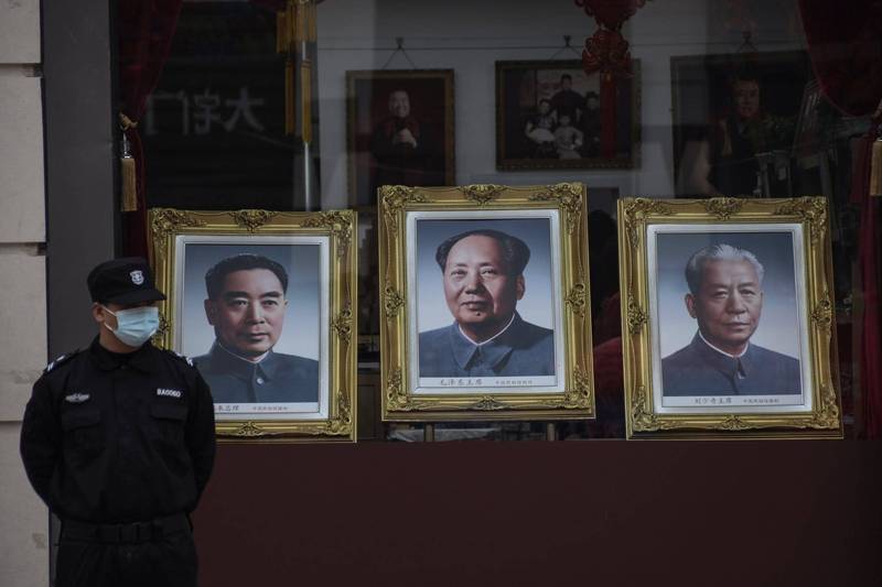 26日是毛泽东（中）128周年冥诞。图中国北京一名保安人员站在王府井大街一间照相馆橱窗前，橱窗内是中共前领导人遗像，中为毛泽东、左为周恩来、右为刘少奇。（欧新社）(photo:LTN)