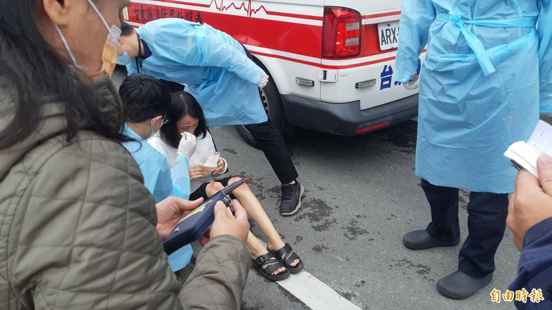 妙齡女子騎機車被狗追，嚇到撞電桿，人受擦傷坐在地上，救護員為她檢視傷勢。（記者黃明堂攝）