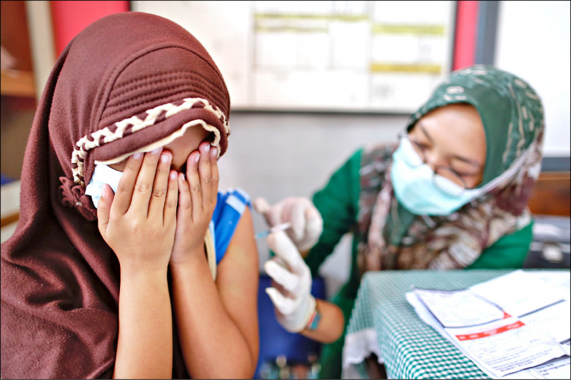 印尼正推動6至11歲兒童接種武肺疫苗，圖為一名小學生在接種中國的「科興」疫苗時，由於緊張而以雙手掩面。（歐新社）