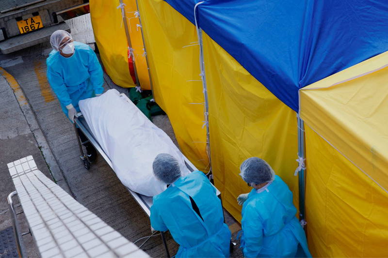 香港部分醫院太平間爆滿，出現遺體堆積情況。圖為穿著防護衣的香港殯儀館員工正在運送遺體。（路透）