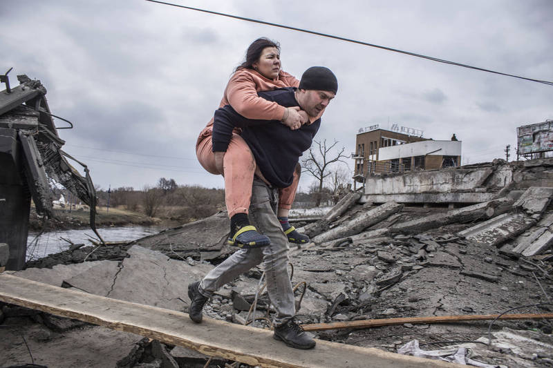 烏克蘭首都基輔西北方的伊爾平市（Irpin）受到戰火摧殘，一名男士協助婦女逃難。俄羅斯方面宣稱，只要烏克蘭政府同意他們開出的條件，雙方就能馬上停火。（美聯社）

