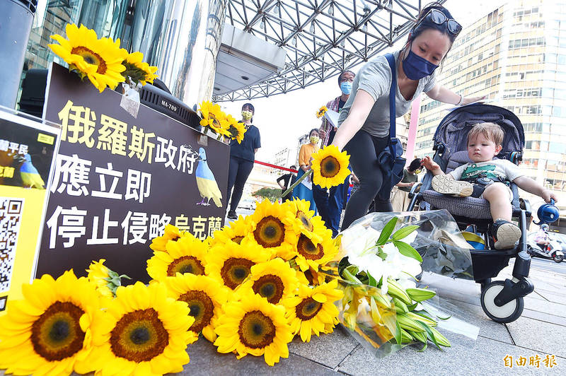 A woman yesterday adds a sunflower to a pile of the flowers in front of a sign that reads: “The Russian government should stop the invasion of Ukraine immediately.” The sign was set up at a news conference and concert organized by Amnesty International Taiwan in front of the Moscow-Taipei Coordination Commission on Economic and Cultural Cooperation in Taipei’s Xinyi District.
Photo: Liao Chen-huei, Taipei Times