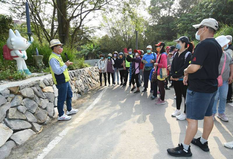 彰化市長林世賢（左）在健行活動起點為民眾解說左邊觀光代言人喵星人-「半半」手拿的就是密毛魔芋。（記者湯世名翻攝）