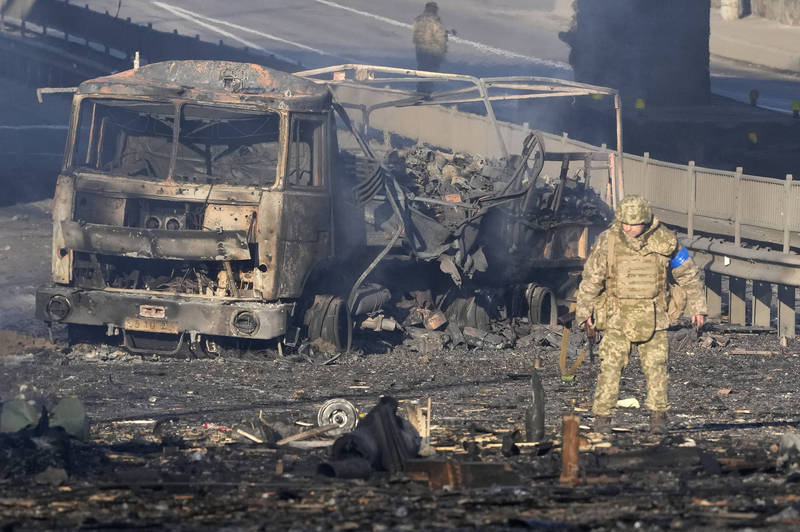 乌克兰士兵正在首都基辅一处公路巡逻，他背后是一辆军用卡车被焚毁的残骸。（美联社）(photo:LTN)