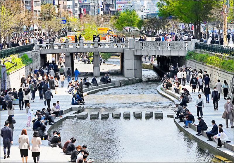 南韓國務總理金富謙宣布，將自十八日起全面解除社交距離措施。圖為十五日在首爾知名景點清溪川的親水河道，可見許多民眾戴口罩散步或坐著。（美聯社）