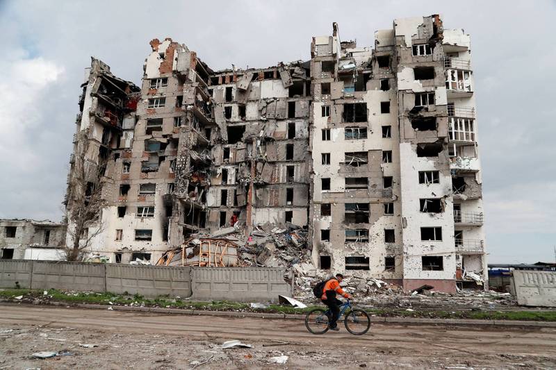 1名男子22日騎車經過烏克蘭南部港口馬立波的一棟已淪為廢墟的住宅大樓。俄羅斯總統普廷21日宣稱已「解放」馬立波。（路透）