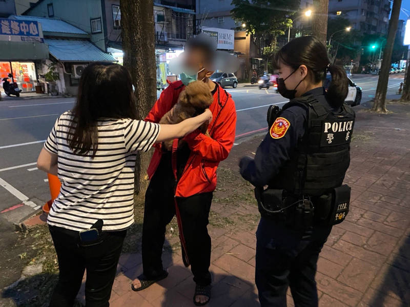 桃市警龜山分局大林派出所門前昨晚上演人狗重聚大戲，羅男（中）前夜帶著懷中的紅貴賓愛犬莎莎外出散步，卻不慎遺失，讓全家人夜不成眠，經向警方求助，終於在地方社團發現好心的林女（左）撿到莎莎並PO網協尋主人，終於讓羅男與莎莎重聚。（記者陳恩惠翻攝）