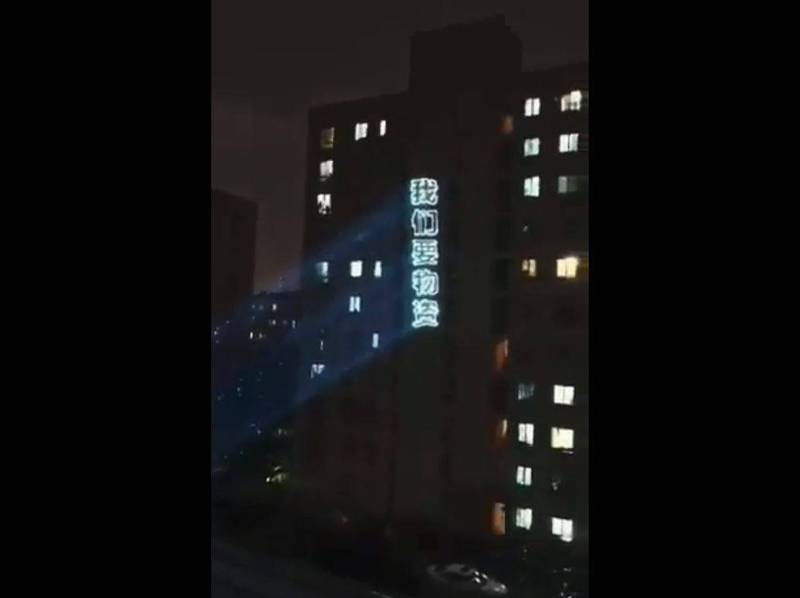 網傳影片中，上海人將「我們要物資」五個大字投影在大樓外牆。（圖取自網路）