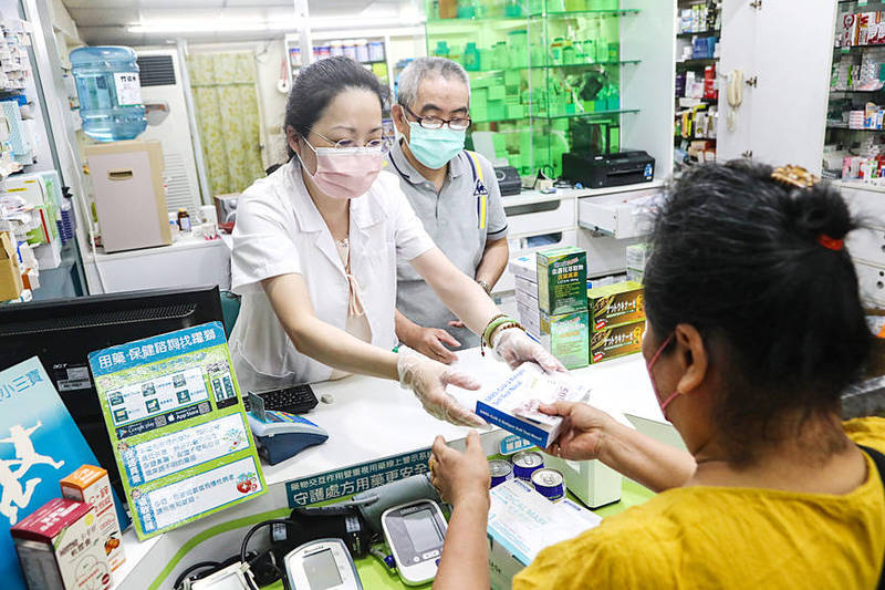 A pharmacist in New Taipei City’s Banciao District hands a customer a COVID-19 rapid test kit yesterday.
Photo: CNA