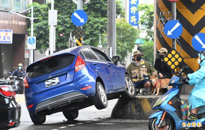 台北市基隆路、東興路與永吉路的十字路口處，今天中午發生一起車禍，藍色小轎車與水泥預拌車發生擦撞後，衝上路中央的行人安全島，小轎車前保桿損毀，右前輪則掛在安全島上，呈現車輛右側前後輪懸空的狀況。（記者田裕華攝）