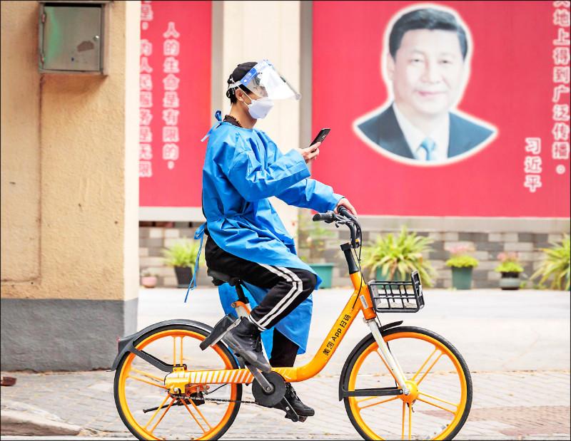 中国国家主席习近平不计代价坚持清零防疫，已引爆广泛民怨。图为上海街头一名全身防护装备的男子骑着单车，廿三日经过吹捧习近平的海报。（欧新社）(photo:LTN)