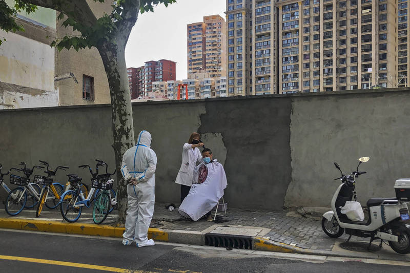 上海市街头，一位理发师正在帮居民理发，另一名身穿防护衣的工作人员在一旁观看。（美联社）(photo:LTN)