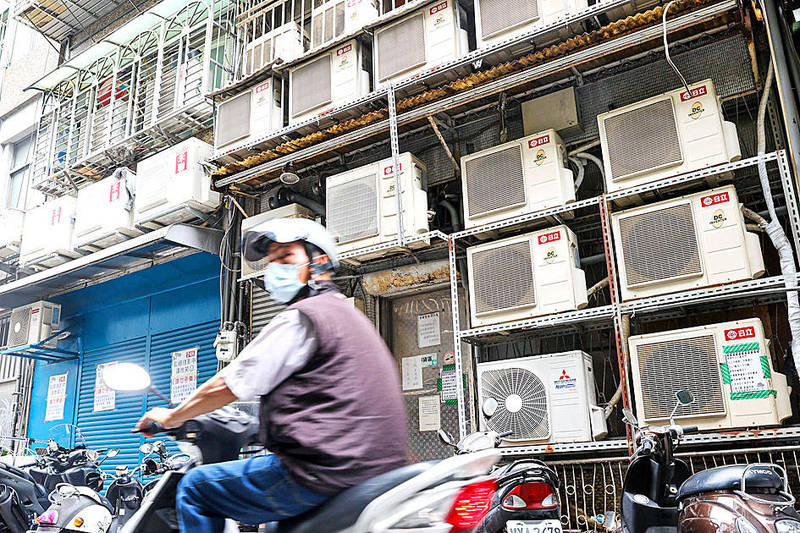 A man on a scooter rides past air-conditioner units outside a building in Taipei on Tuesday.
Photo: CNA