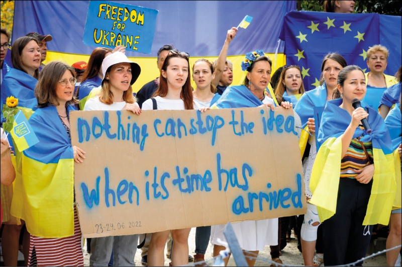 披著藍、黃色烏克蘭國旗的抗議人士，23日舉著寫有「時候到了」的英文標語，在歐盟峰會布魯塞爾會場外要求歐盟成員國領袖同意烏克蘭入盟。（歐新社）