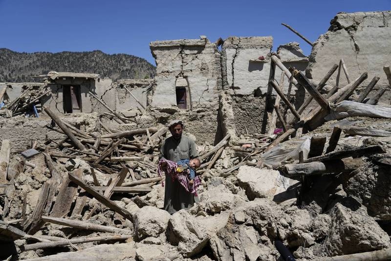 1名阿富汗男子24日抱著孩子站在遭日前強震摧毀的廢墟中。（美聯社）