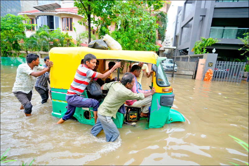 印度民眾在淹水的道路上推著一台三輪車。（美聯社）