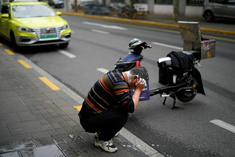 5月上海封城期间，一名因封锁措施无法回家的送货员在公车站生活，图为送货员在路旁洗发。（路透）(photo:LTN)