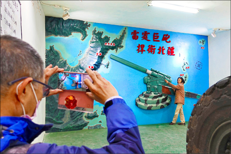 觀光客在馬祖南竿的戰地文化博物館裡，與寫有「雷霆巨砲 捍衛北疆」的壁畫合影。（美聯社）